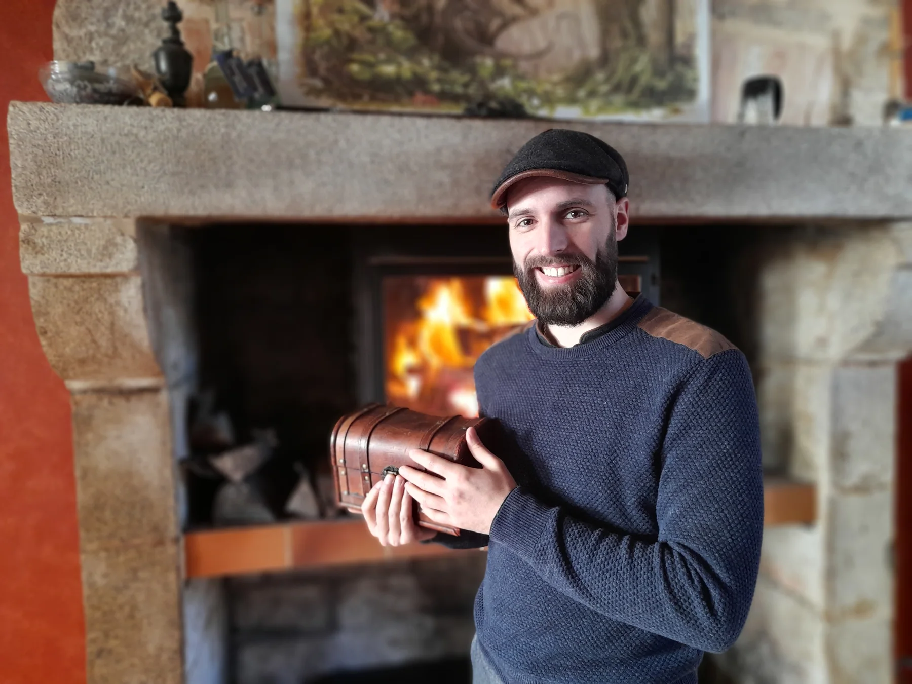 Jack Audefroy souriant, un petit coffre entre les mains, devant une cheminée